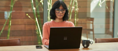A woman in a red shirt and glasses working on a laptop.