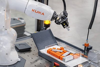 A robotic arm holding a box containing orange objects with KUKA text visible.