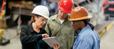 A group of people wearing hard hats looking at a tablet.
