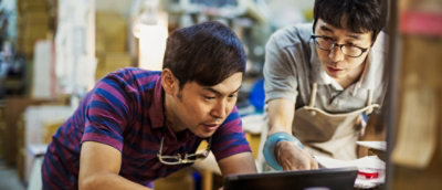 Two craftsmen in a workshop examining a piece closely.