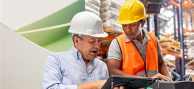 Two men wearing hard helmets, looking at a tablet.