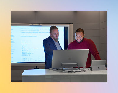 Deux hommes se tiennent ensemble dans un bureau moderne, regardant un écran d’ordinateur et souriant. 