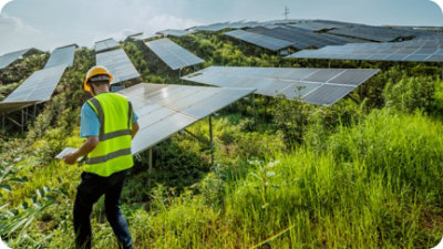 Une personne disposant d’un casque et d’un gilet à visibilité élevée inspecte une butte avec plusieurs panneaux solaires installés.