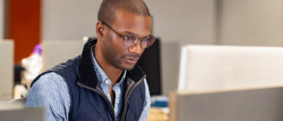 En mand med briller og en vest kigger ned på en computer.