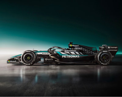 Mercedes-AMG PETRONAS Formula One race car in side profile on a reflective surface with a teal gradient background.