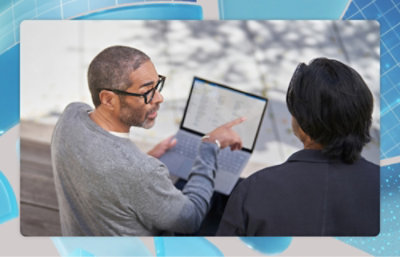 Two people sitting outside talking while one holds a laptop