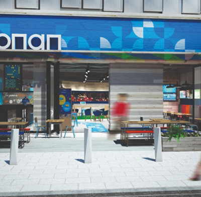 Vue extérieure d'un restaurant moderne avec une marque colorée, des places assises en extérieur et des piétons flous passant.