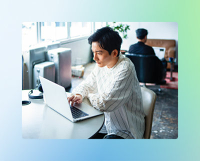 Une personne portant une chemise rayée travaille sur un ordinateur portable à une table dans une pièce bien éclairée.