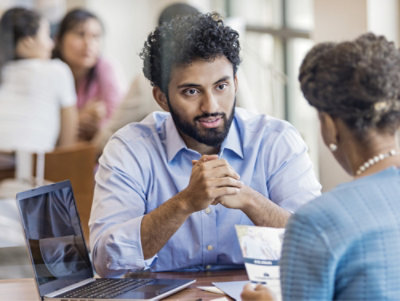 A man with curly hair and a beard sitting at a table.