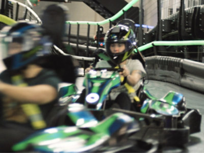  Child riding a go-kart in full helmet gear or an indoor track.