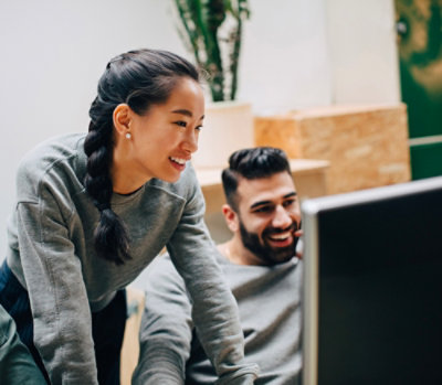 Team collaborating at a workstation while reviewing content on a large desktop monitor in an office setting.