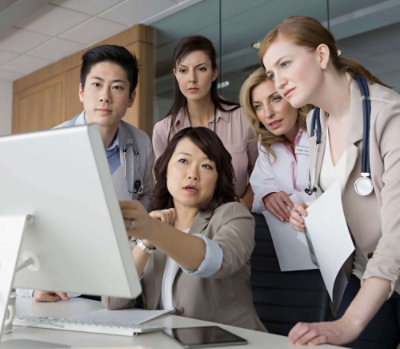 Medical professionals collaborating around a computer while reviewing clinical information in a hospital setting.