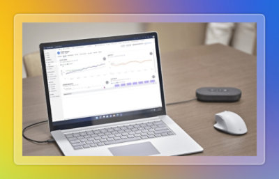 Laptop on a desk displaying analytics and performance charts next to a mouse and smart speaker.