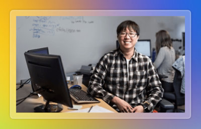 An employee with computer besides him smiling towards camera.