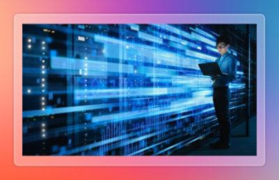  IT professional monitoring and managing data flows across illuminated server racks using a laptop in a data center.