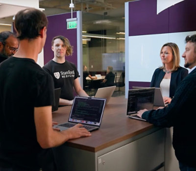 Group collaborating at a standing counter while reviewing work on laptops in a modern office workspace.