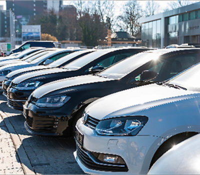 Line of parked cars in an outdoor lot near modern commercial buildings.