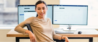 A woman looking at the camera sitting infront of desktop setup