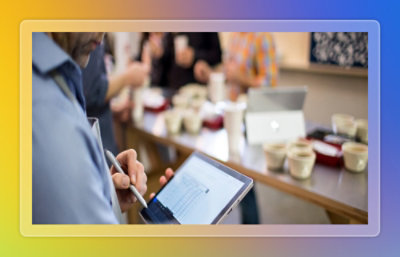 Person reviewing tabular data on a tablet during a collaborative work session with laptops and documents on a table.