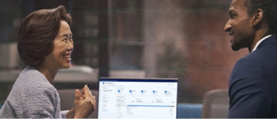 Zwei Beschäftigte in einem modernen Büro lächeln, während sie etwas besprechen, das auf dem Computerbildschirm zwischen ihnen angezeigt wird.