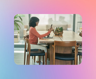 Een persoon die aan een tafel zit en naar haar telefoon kijkt