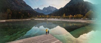Několik lidí, kteří stojí na molu s výhledem na jezero s horami a stromy v pozadí.