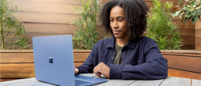 Person using a laptop at an outdoor table with greenery.