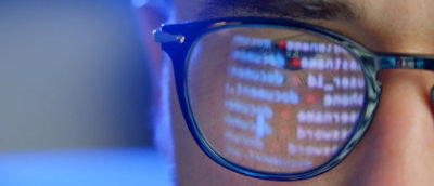 Close-up of glasses reflecting lines of code on a screen.