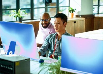 Two people collaborating at desktop computers in a bright office.