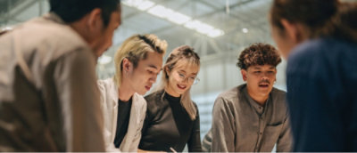 A group of people are gathered around a table. They appear to be engaged in a discussion or collaboration.