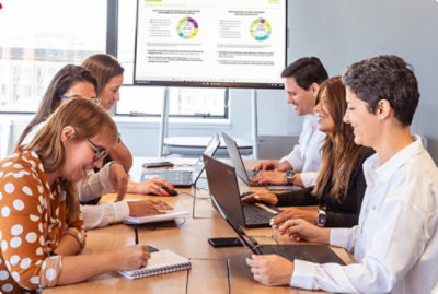 A group of people sitting around a table with laptops