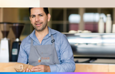 A man in a grey apron holding a bag of coffee.