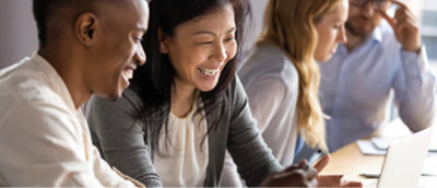 Four people sit at a table, engaged in conversation and looking at a laptop.