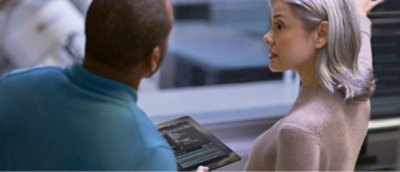 两个人正在屏幕前讨论，其中一人拿着一个显示信息的平板电脑。