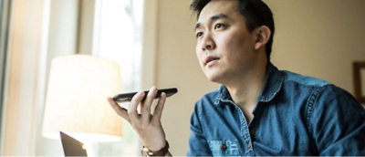 Un hombre con una camiseta denim sujeta un smartphone en la boca y parece hablar o grabar un mensaje. 