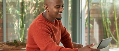 A person using tablet and smiling with coffee and fruits placed on the table