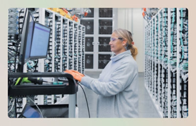 A person works on a computer in a room filled with server racks.