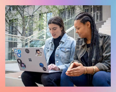 A couple of women sitting on stairs looking at a computer.