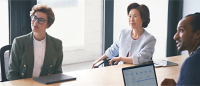 Tre personer sidder ved et konferencebord og deltager i et møde.