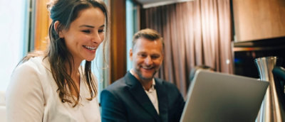 A man wearing glasses and a green jacket looking at a laptop.