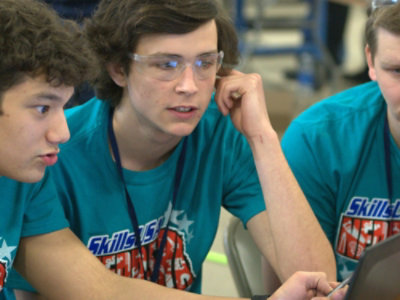 黄色のパーカーを着た人が笑顔で、プレゼンテーションのスライドを表示するタブレットを持っています。