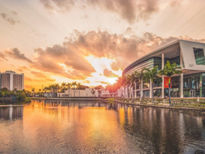 フロリダ州マイアミの見事なアーキテクチャと落ち着いた水に沈む夕日、鮮やかな雲と湖に映るヤシの木。
