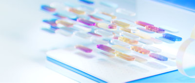 Cápsulas coloridas e transparentes de vários tamanhos pairam sobre um fundo claro, criando uma composição futurista e abstrata.