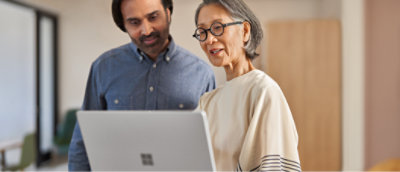 Duas pessoas estão próximas, olhando para a tela de um laptop. A pessoa à esquerda usa uma camiseta azul
