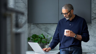 Um homem digita em um laptop enquanto segura uma xícara