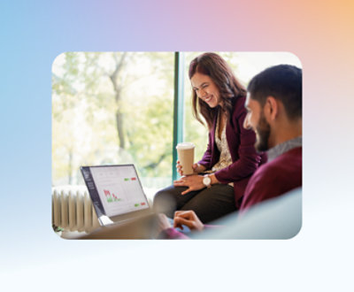 Duas pessoas sentadas em um sofá, olhando para um laptop. Um segura uma xícara de café e está sorrindo, enquanto o laptop mostra um gráfico.