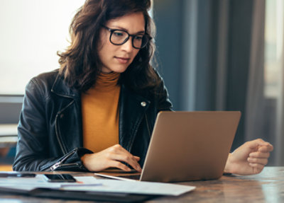 A woman in glasses looking at a laptop.