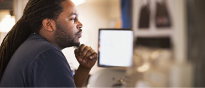 A man with long hair and a ponytail looking at a computer screen.