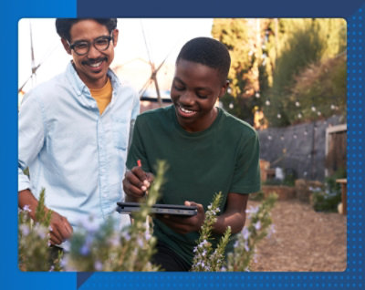 Two smiling young men using a tablet and stylus in a garden setting.