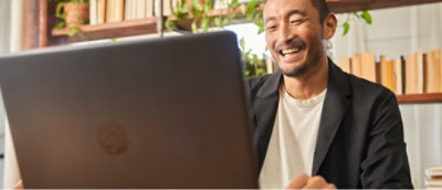 Person using a laptop at home office with books and plants in the background.